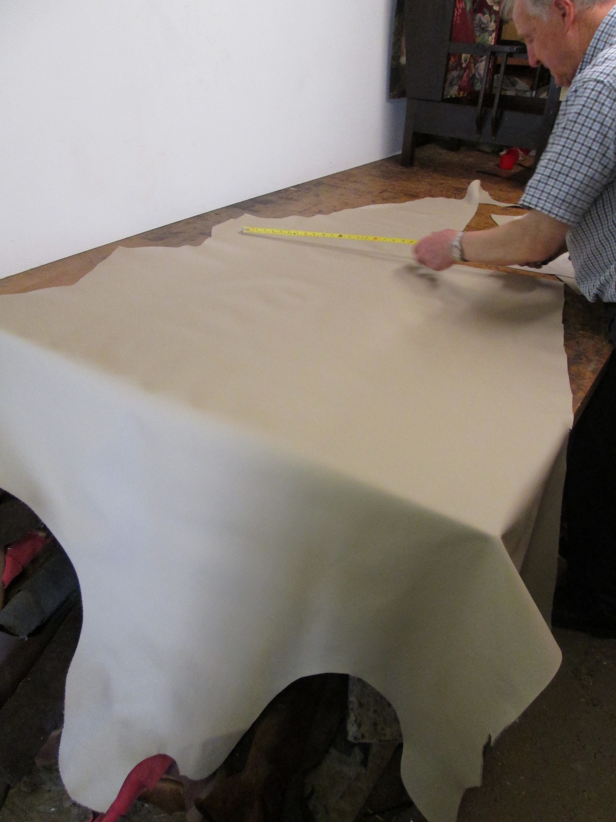 Measuring out a cream leather hide on the workshop bench