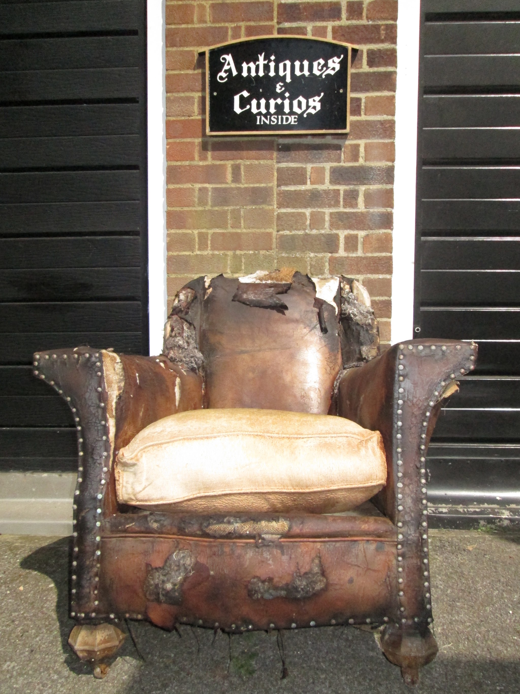 A worn studded leather armchair outside the workshop, under an Antiques and Curios sign
