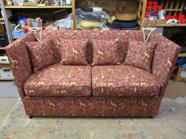 A Knole sofa in red patterned fabric in the workshop, with shelves of fabric behind